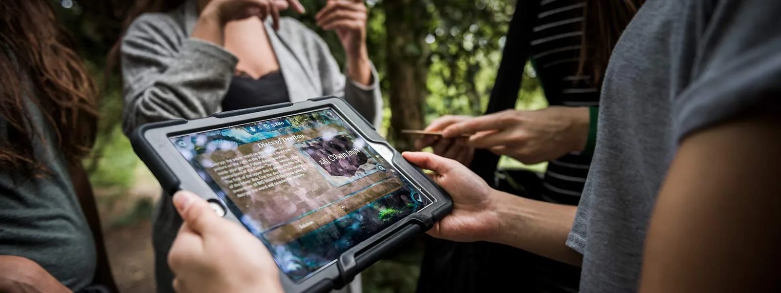 Team liest einen Hinweis auf dem iPad bei einem Outdoor Escape Game im Park