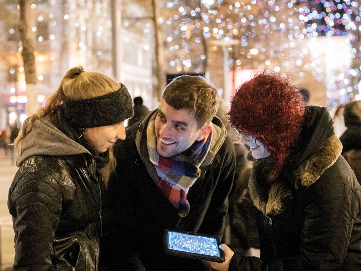 Team building de Noël : des collègues résolvent une énigme sur tablette sous les guirlandes lumineuses